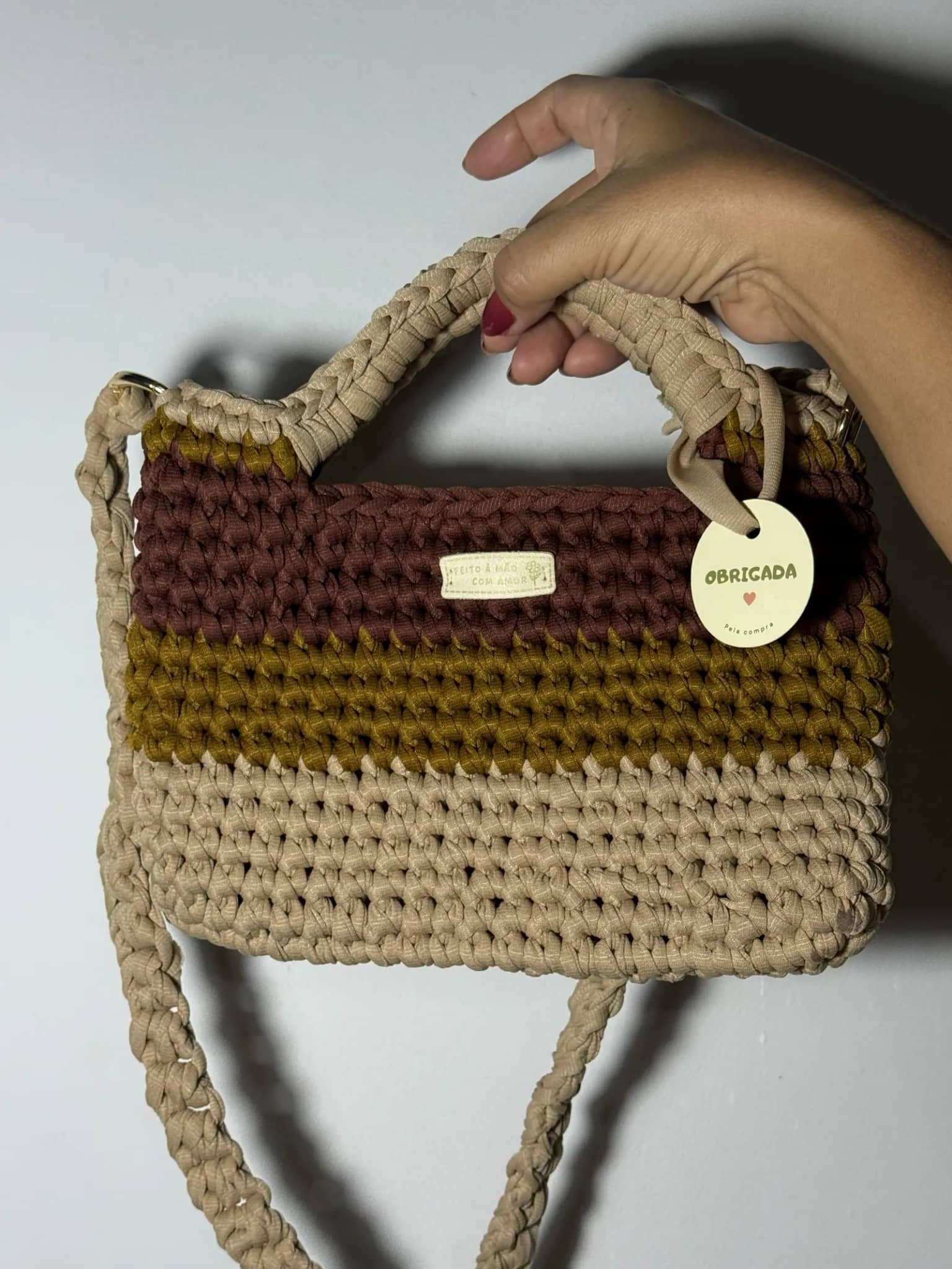Bolsa de crochê em faixas marrom, mostarda e bege, com alça de mão trançada e alça longa