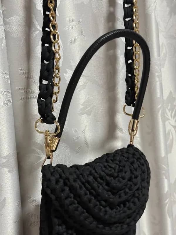 Bolsa preta com aba pendurada, mostrando a alça e a corrente