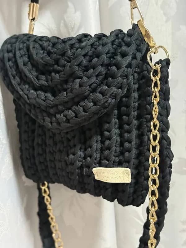 Detalhe da aba em relevo e da plaquinha da bolsa preta