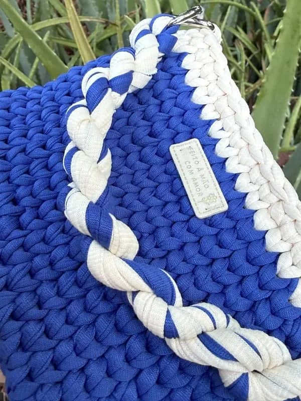 Detalhe da alça trançada azul e branca e da plaquinha da bolsa