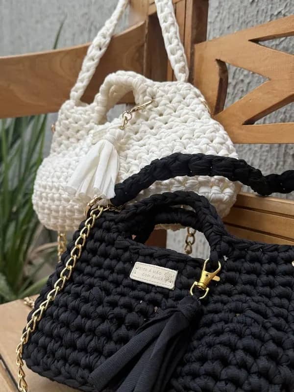 Bolsas de crochê preta e cru com tassel, sobre banco de madeira