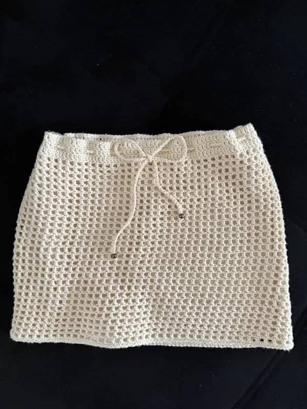 Saia curta de crochê cru de trama aberta, com cordão na cintura