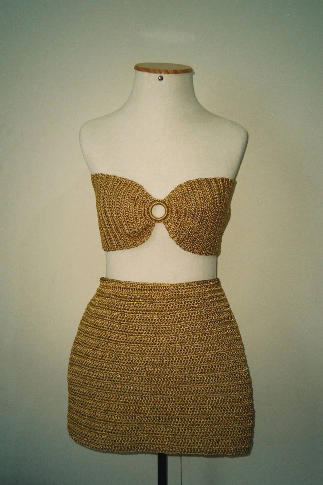 Conjunto de crochê dourado com top tomara que caia com argola e saia curta, no manequim, visto de frente