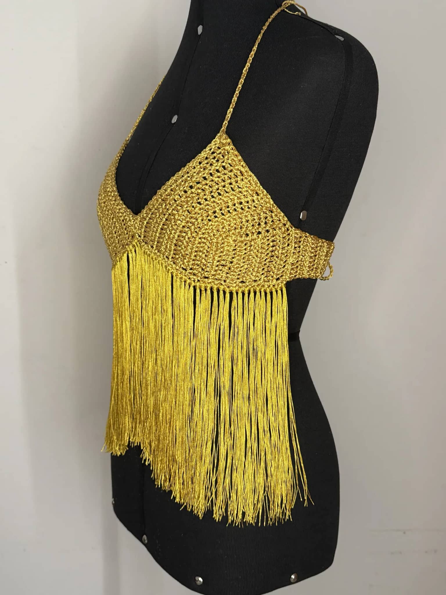 Cropped halter dourado com franjas longas, visto de lado no manequim preto