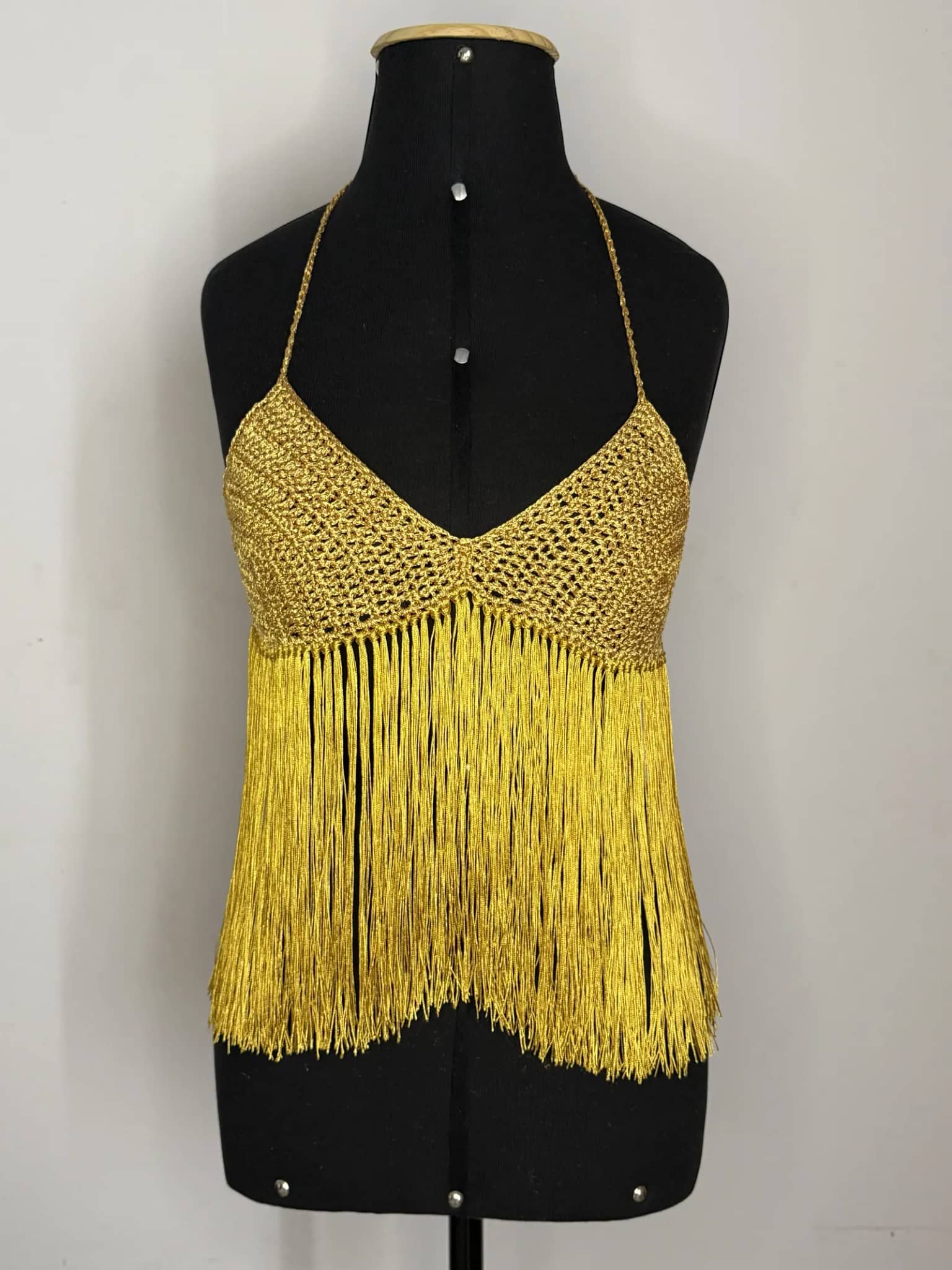 Cropped halter dourado com franjas longas, visto de frente no manequim preto