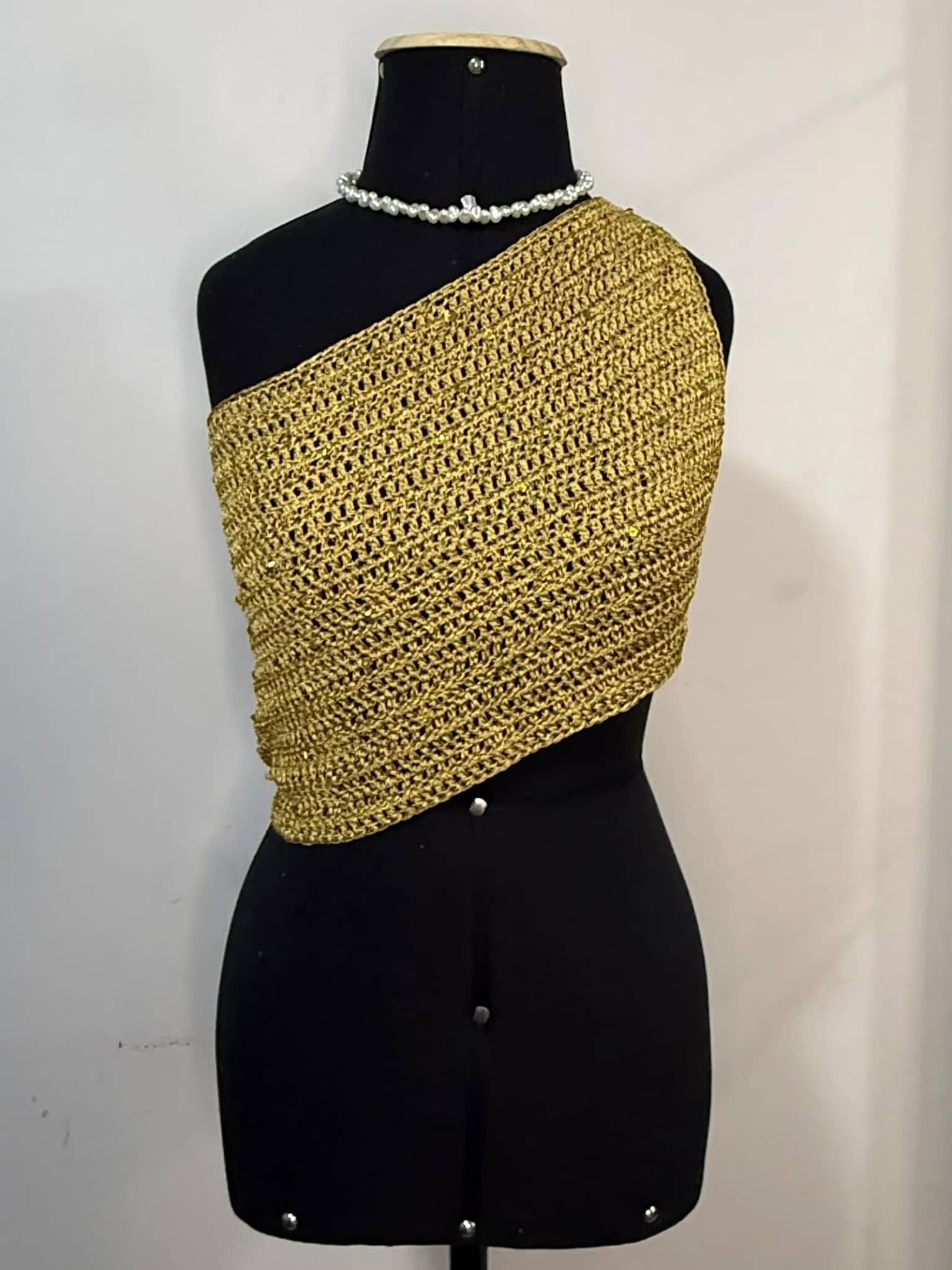 Cropped assimétrico dourado de um ombro só, no manequim preto com colar de pérolas