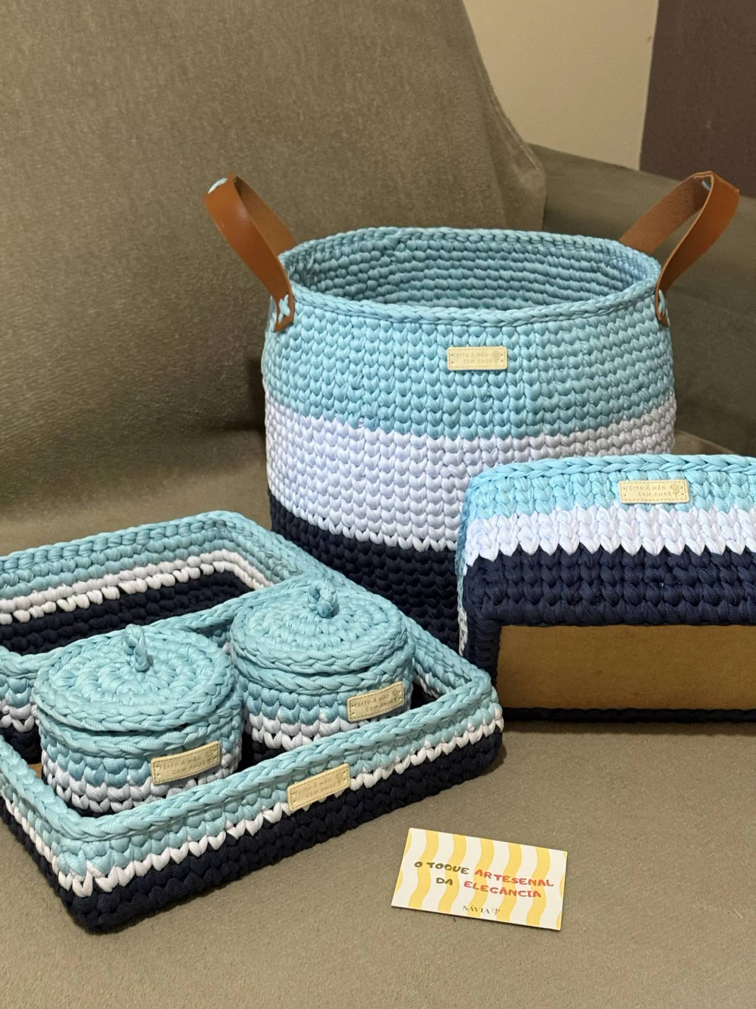 Kit completo de crochê azul, branco e azul-marinho sobre o sofá, com o cartão da Sávia