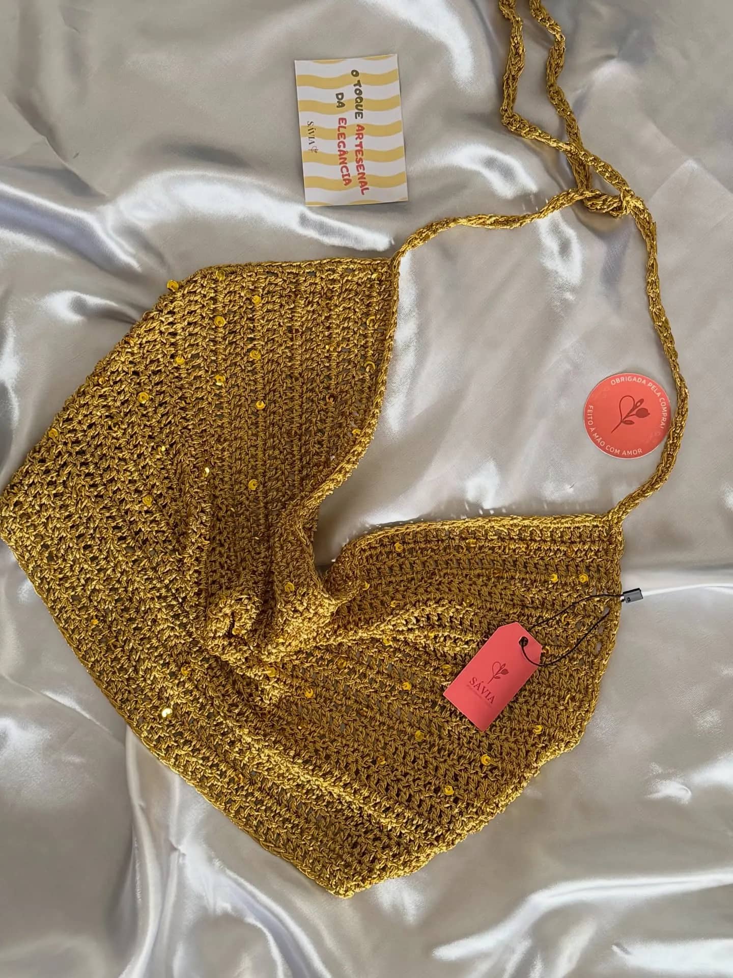 Top lenço de crochê dourado sobre tecido acetinado, com etiqueta rosa da Sávia