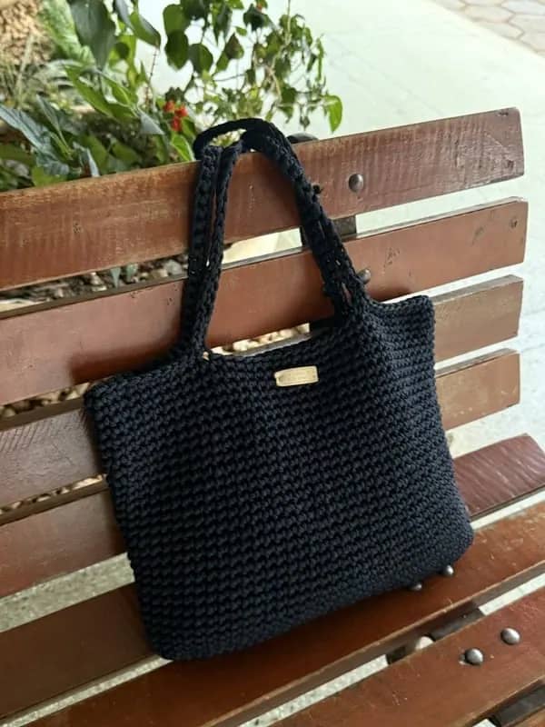 Bolsa tote de crochê preta apoiada em um banco de madeira