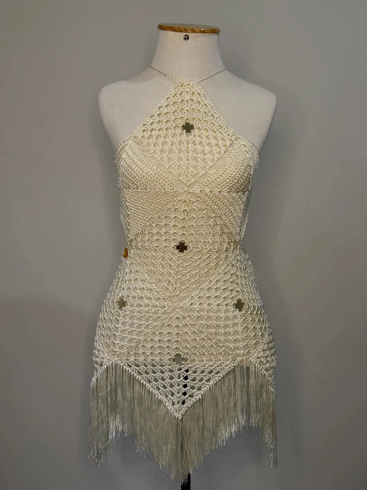 Vestido curto de crochê creme em trama aberta com franjas na barra, no manequim